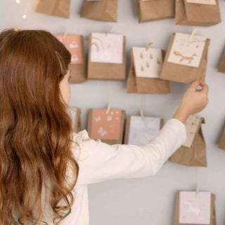 Mädchen greift nach brauner Papiertüte mit Meerjungfrauenmotiv, Teil eines DIY-Adventskalender-Sets; ideal zum Befüllen.