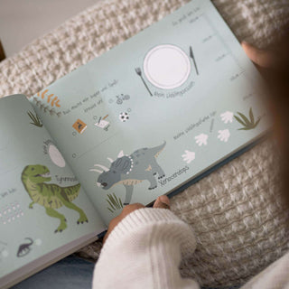 Ein Kind betrachtet ein Freundebuch mit Dinosaurierbildern, darunter ein Tyrannosaurus Rex und ein Triceratops in kräftigen Farben.