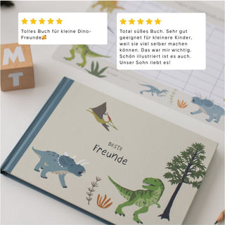 Kinderfreundebuch "Dinosaurier" auf einem Tisch liegend mit zwei Kundenbewertungen. Buchstabenwürfel und Stundenplan liegen daneben.