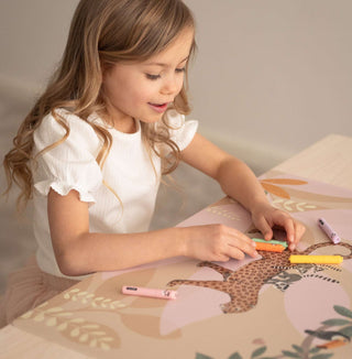Ein Kind spielt mit Buntstiften auf einer Kinderschreibtischunterlage. Dort sind versielte Lemuren, einen freundlichen Leopard und viele weitere lustige Tiere  künstlerisch dargestellt. Wunderschöne Farbkombination aus Pastell und kräftigen Farben im Hintergrund unterstreichen die fantastische Welt des Jungels.