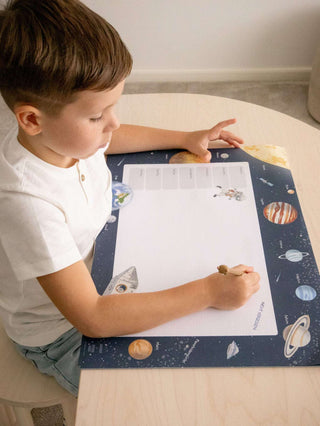 Ein Kind sitzt an einem Kinderschreibtisch und malt auf einer großen Papierblockunterlage mit Space Design.