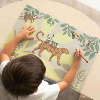Ein Kind sitzt an einem Kinderschreibtisch auf dem eine Schreibtischunterlage mit Jungle Design liegt. Verspielte Lemuren, einen coolen Leopard und viele weitere lustige Tiere sind auf dieser abwaschbaren Unterlage künstlerisch dargestellt. Wunderschöne Farbkombination aus natürlichen und kräftigen Farben im Hintergrund unterstreichen die fantastische Welt des Jungels.