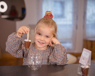 Ein kleines Mädchen zeigt glücklich eine Trinkschokolade am Holzstil hoch