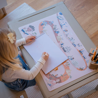 Mädchen malt auf rosa Schreibtischunterlage Zeitreise: Von oben fotografiertes Mädchen, das auf einem Zeichenblock auf der rosafarbenen Lernmatte "Zeitreise der Menschheit" am Kindertisch kreativ wird. Kreativspiel und Geschichtslernen.