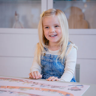 Vorschulkind strahlt beim Entdecken der rosafarbenen Schreibtischunterlage "Zeitreise der Menschheit", Lernspielzeug, pädagogisches Kindergeschenk.
