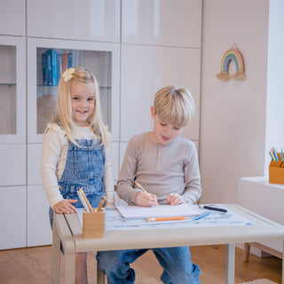 Pädagogische Schreibtischunterlage für Kinder: Zwei Kinder erkunden die detaillierte Zeitreise-Illustration auf der großen, blauen Lernmatte am Kindertisch. Perfekt für spielerisches Geschichtswissen.