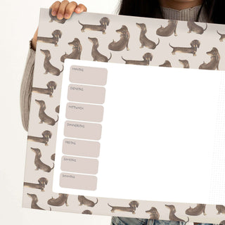 Papierblockunterlage im skandinavischen Stil, illustriert mit Dackeln. Wochenplaner mit beschrifteten Wochentagen am Rand.