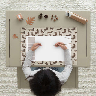 Papierblockunterlage im skandinavischen Stil mit Dackelmotiven, Herbstlaub und Nüssen. Kind schreibt einen Wochenplan.
