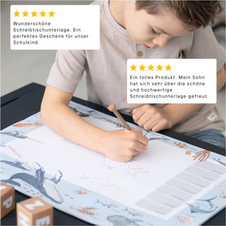 Ein Kind schreibt auf einer Schreibtischunterlage mit Meerestieren, ideal für Schulstart, Geschenkidee, Jungen und Mädchen. Es sind zwei Kundenbewertungen abgebildet.