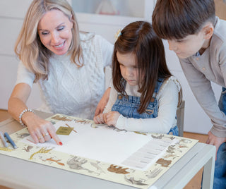 Eine Frau zeigt zwei Kinder die Kinderschreibtischunterlage Tier ABC. Jedes Tier ist mit seinem Namen und dem dazu passenden Buchstaben dargestellt. 