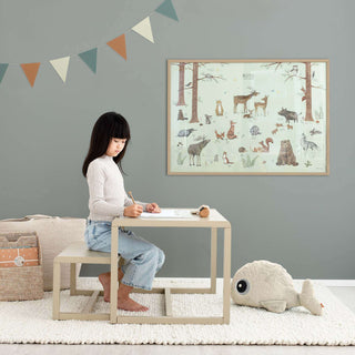 Kind sitzt am Tisch im Kinderzimmer, zeichnet, "Waldtiere" Poster mit grünen Waldtieren an der Wand, naturfreundlich.