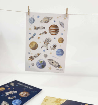 Blatt mit transparenten Weltraumaufklebern mit Planeten, Astronauten, Sternen, Raketen und Satelliten, aufgehängt an einer Wäscheleine.