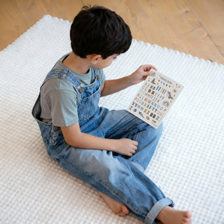 Ein Kind betrachtet den Alphabet-Sticker, Titel "SCHULKIND", bunte Buchstaben, verspielte Illustrationen, transparente Sticker, in seiner Hand.