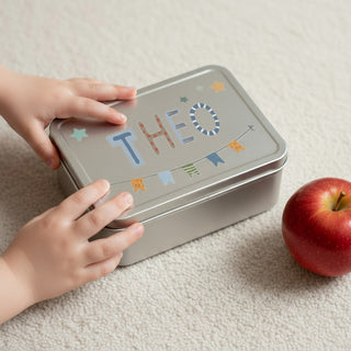 Eine Blechbrotdose mit Namen einen Kindes mit Buchstabenstickern und Wimpelgirlande individuell dekoriert.