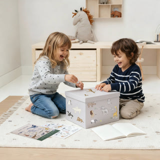 Zwei Kinder sitzen in einem minimalistischen Kinderzimmer und bekleben lachend eine Kisten mit Tier-Stickern.