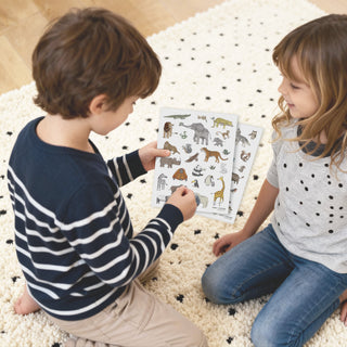 Zwei Kinder sitzen auf dem Boden. Der Junge zeigt dem Mädchen zwei Tierstickerbögen von dem Tiersticker Set "Entdecke die Wildnis!"