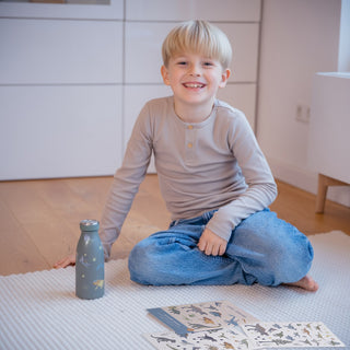 Ein Junge schaut lachend in die Kamera. Seine Trinkflasche ist mit den Dino-Sticker vom Mega Dino-Sticker Set beklebt.