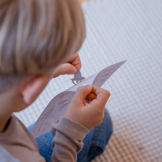 Ein Kind zieht einen Dino-Sticker mit transparentem Hintergrund vom Bogen.