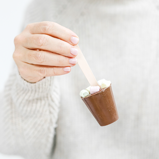 Milchschokolade mit bunten Marshmallows am Holzstil in einer Hand.