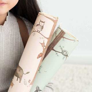 Ein Kind hält zwei abwaschbare Schreibtischunterlagen mit Waldtieren im neutralen Design, darunter Eule, Fuchs und Baum.