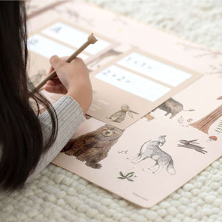 Schreibtischunterlage mit Waldtieren, darunter Bär und Wolf, auf beigem Hintergrund; Kind zeichnet darauf.