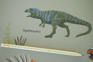 Schreibtischunterlage mit Dinosaurier-Motiv, zeigt einen Gigantosaurus mit Pflanzen. Ein Bleistift liegt auf der Unterlage.