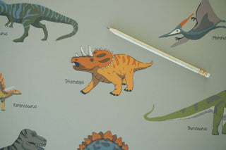 Bunte Schreibtischunterlage für Kinder zeigt acht Dinosaurier, darunter Triceratops und Pteranodon, mit Bleistift als Maßstab.