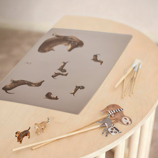 Taupefarbene Schreibtischunterlage mit Dackeln in spielerischen Posen, abwaschbar, ideal für Liebhaber der Hunderasse Dackel. Auf einem Kinderschreibtisch plaziert. Kleine Tierfiguren  und Pinsel liegen daneben.