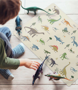 Ein Kind sitz auf dem Boden und spielt mit Spielzeug Dinosauriern und einer ABC Dino Schreibtischunterlage