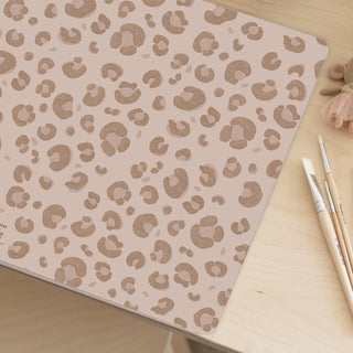 Leopardenmuster-Schreibtischunterlage, abwaschbar, auf Holzschreibtisch, mit Pinsel daneben.