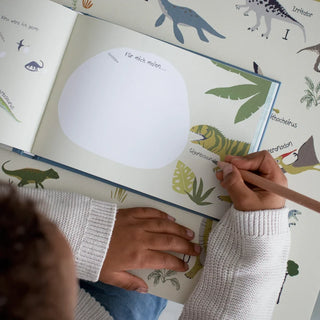 Kind malt in einem Dinosaurier-Aktivitätsbuch; bunte Dinosaurierillustrationen umgeben die leeren Zeichenseiten.