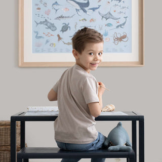 Ein Kind sitzt an einem Tisch und zeichnet, mit einem Meerestiere-Poster im Hintergrund, 60x80 cm, Lernposter für Kinder.